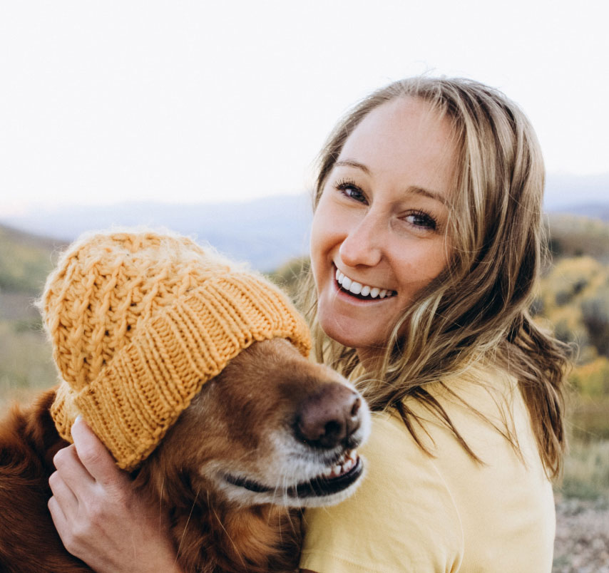 Woman and her dog posing for a picture. A beanie hat is on the dogs head.
